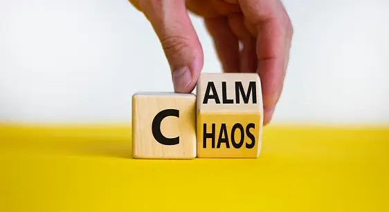 two wooden blocks, one with a C and the other partially being turned by a human hand with one side saying 'alm' and the other 'haos' To signify the benefits of coaching - from chaos to calm.